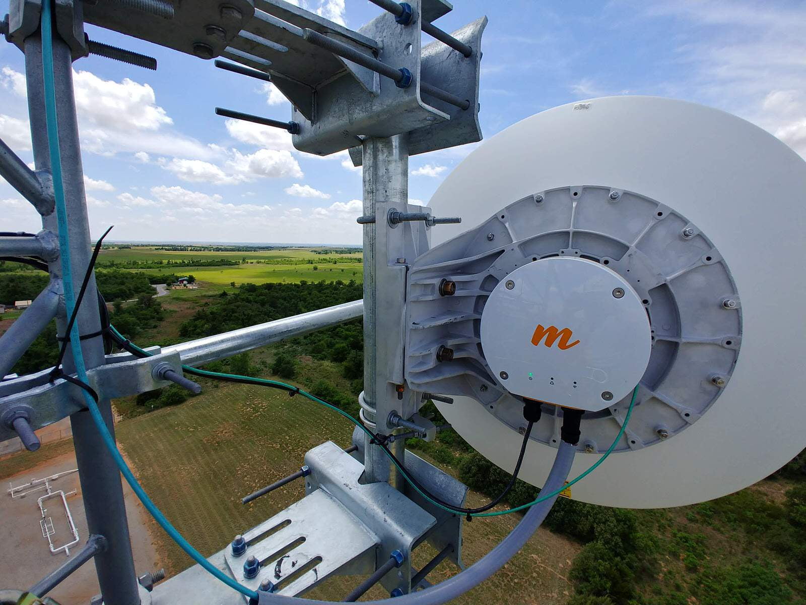 Backhaul dish mounted and aligned on a communications tower high above open farmland