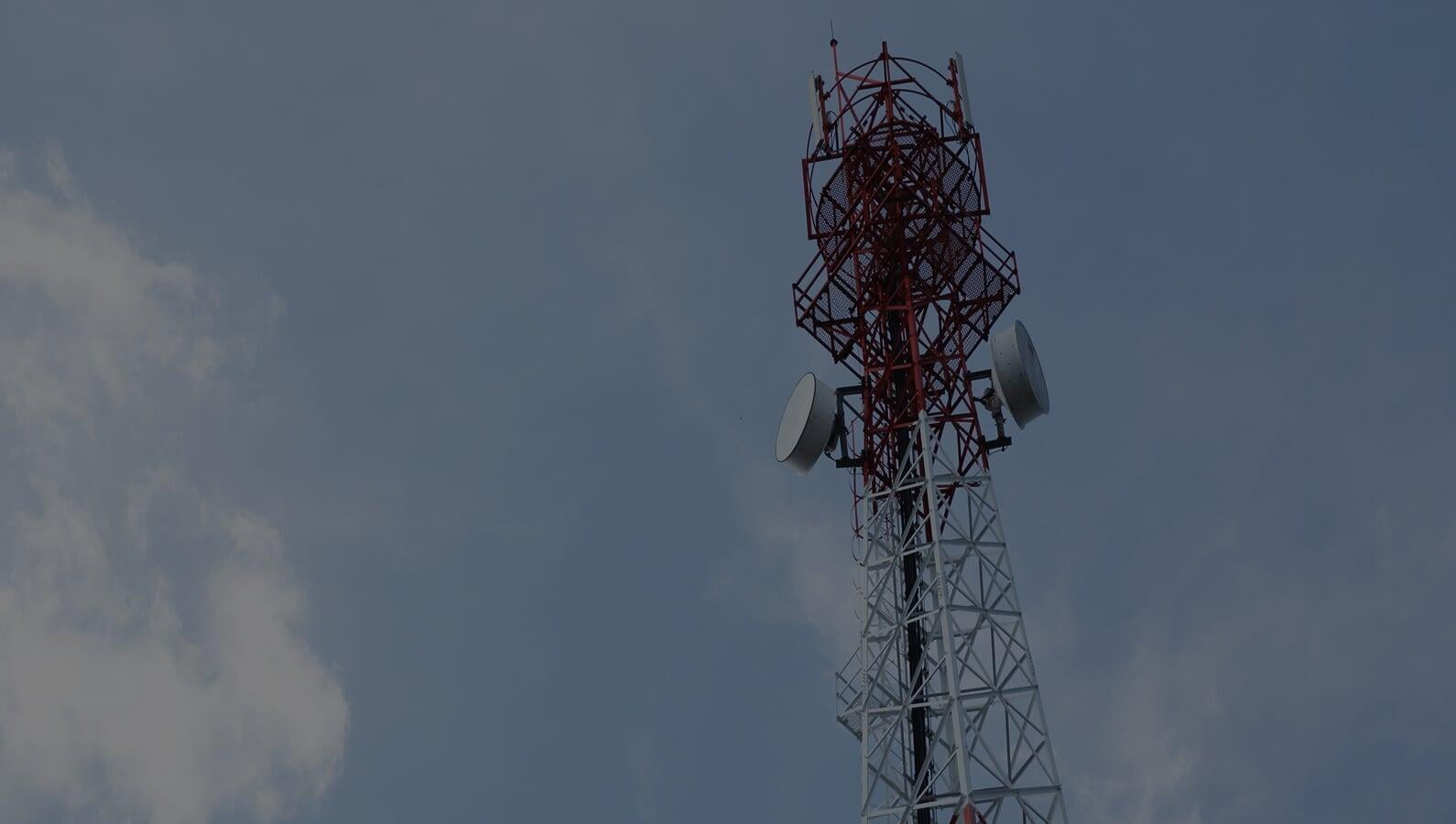 Lattice communications tower carrying microwave dishes and panel antennas against an overcast sky