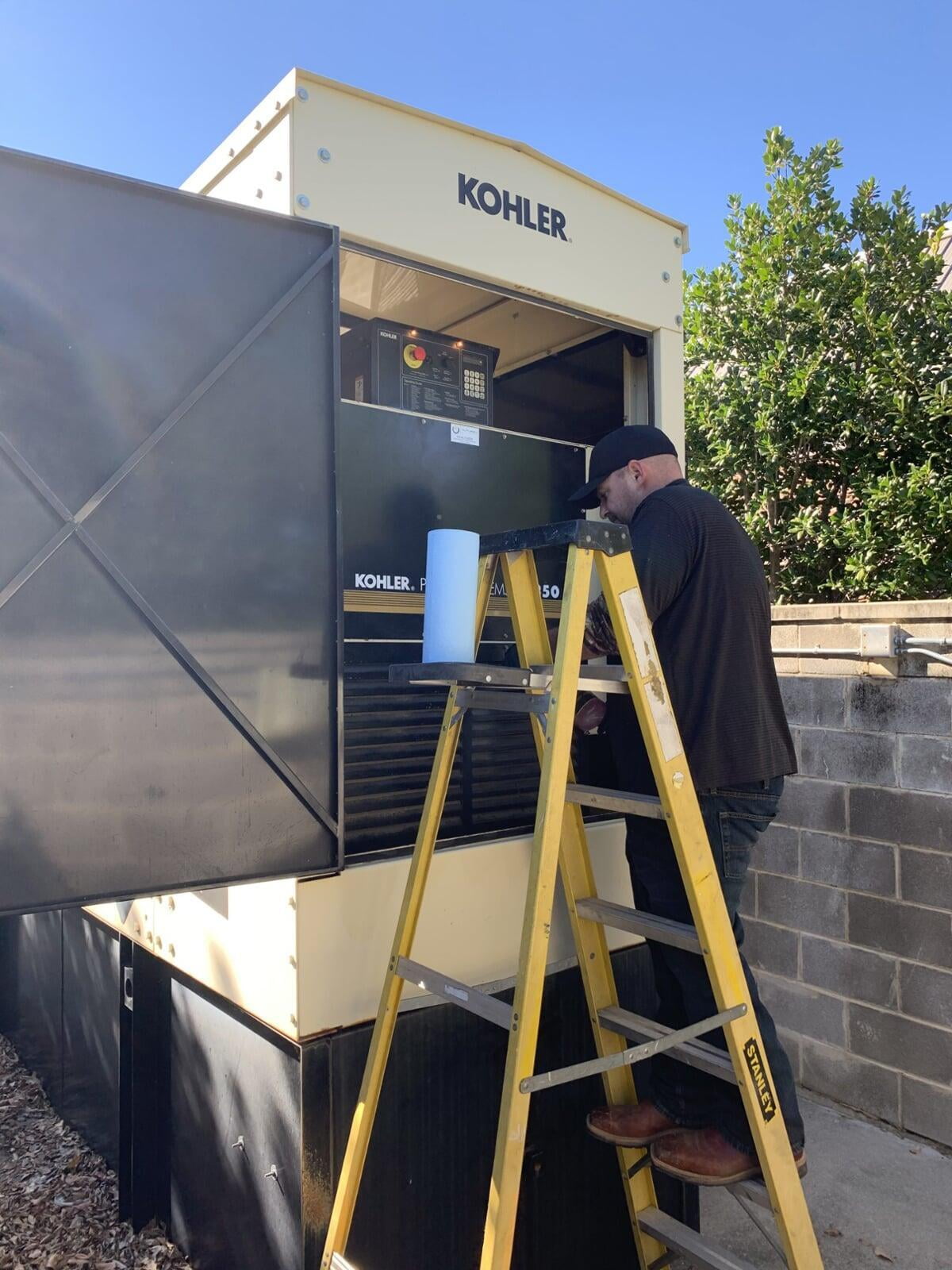 Alturex technician on a step ladder servicing an open Kohler standby generator