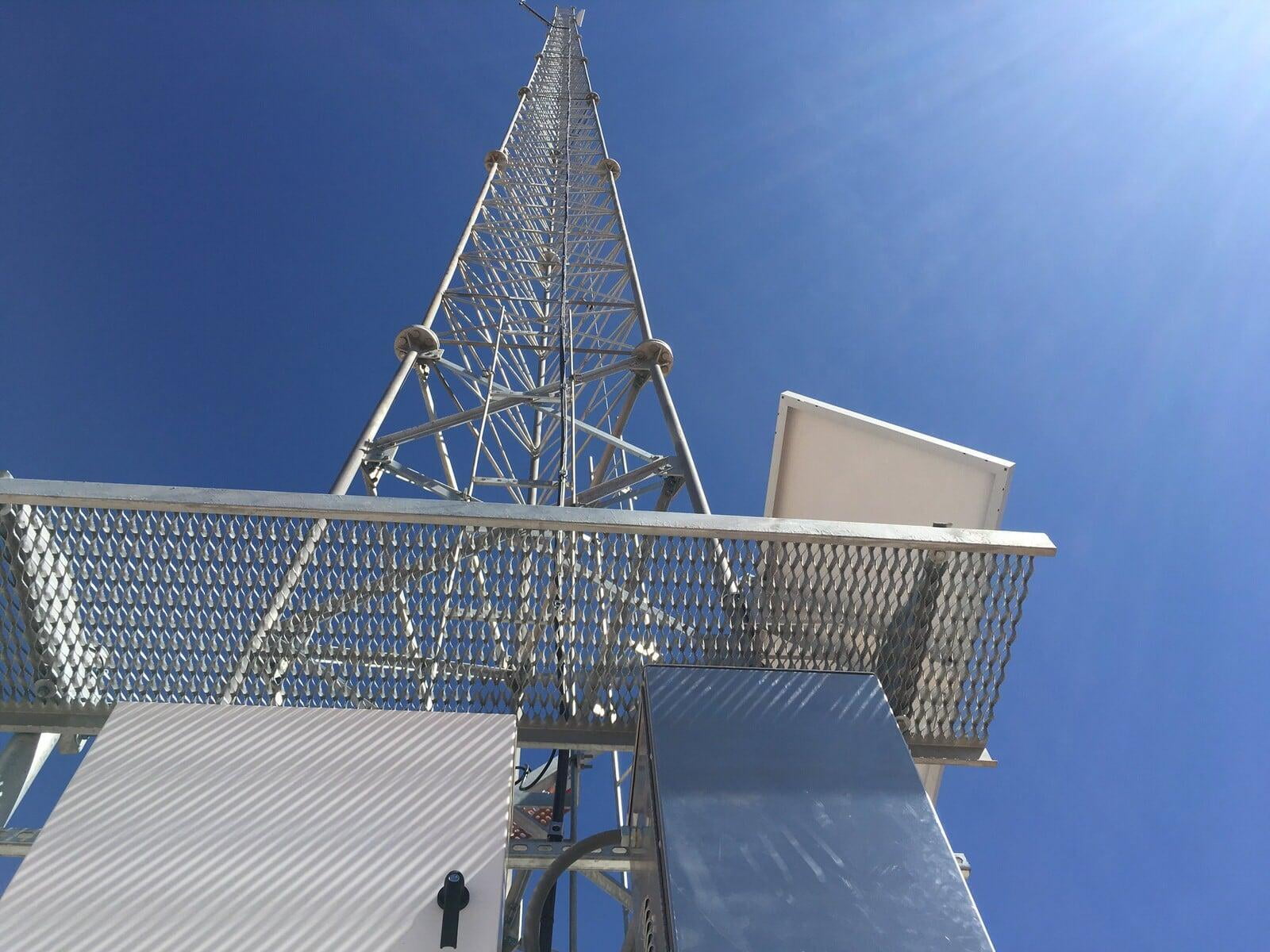 Communications tower with solar-powered equipment cabinets against a clear blue sky